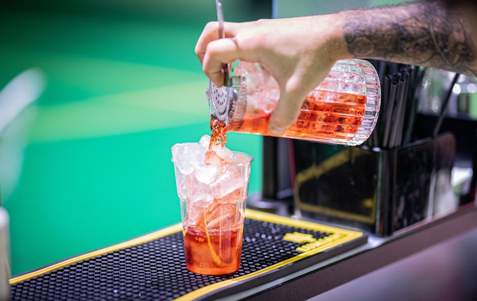 Close-up of bartender pouring a red cocktail into a glass filled with ice.