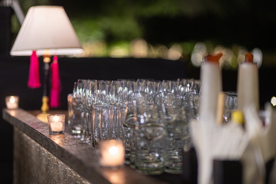 An elegant outdoor bar setup at night featuring empty glasses, candles, and ambient lighting.