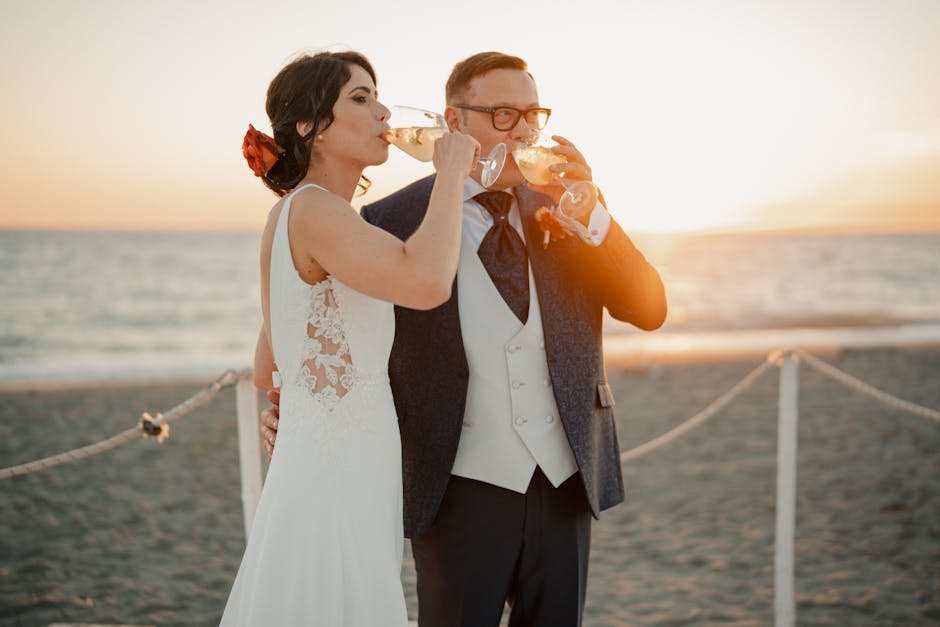 Bride and groom share a joyful sunset toast on the beach, celebrating their wedding day in style.
