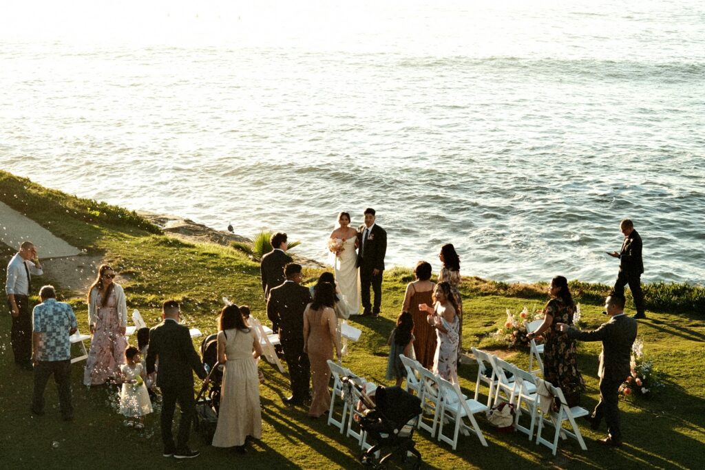 A beautiful seaside outdoor wedding ceremony at sunset with guests and a lovely setting.