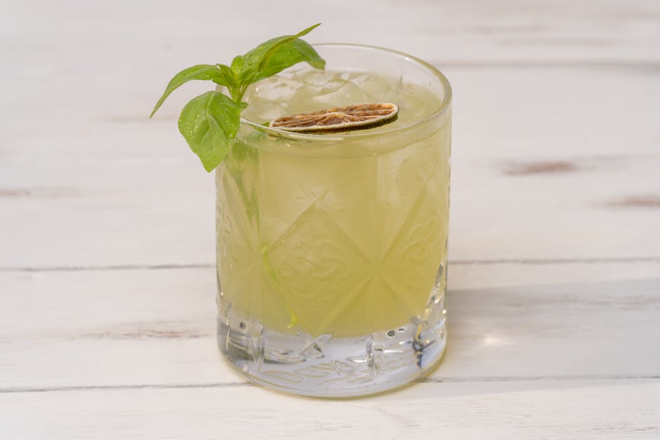 Cool lime cocktail with mint garnish served in a patterned glass on a wooden table.